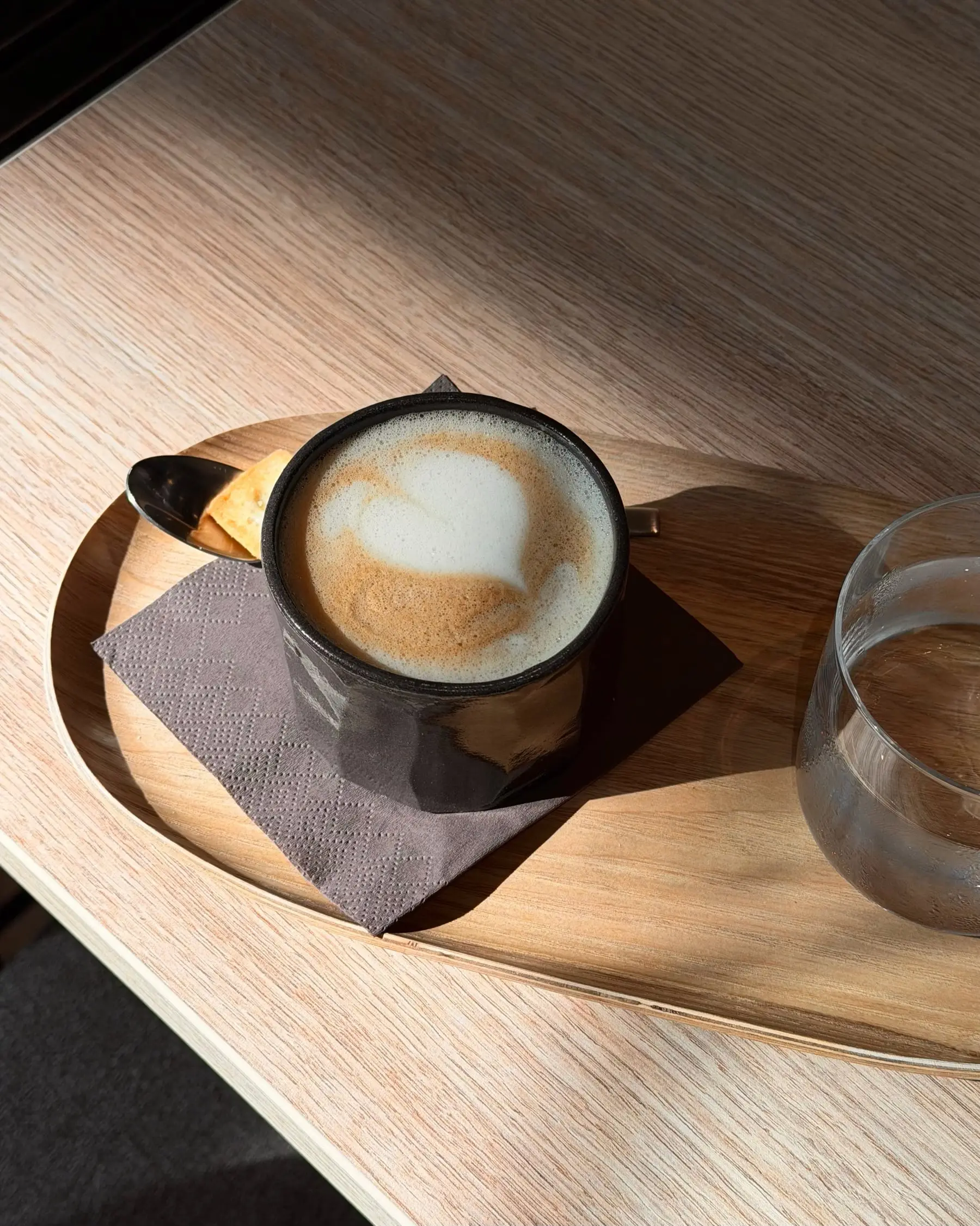 Cappuccino mit Latte Art in einer dunklen, handgetöpferten Tasse auf einem Holztablett