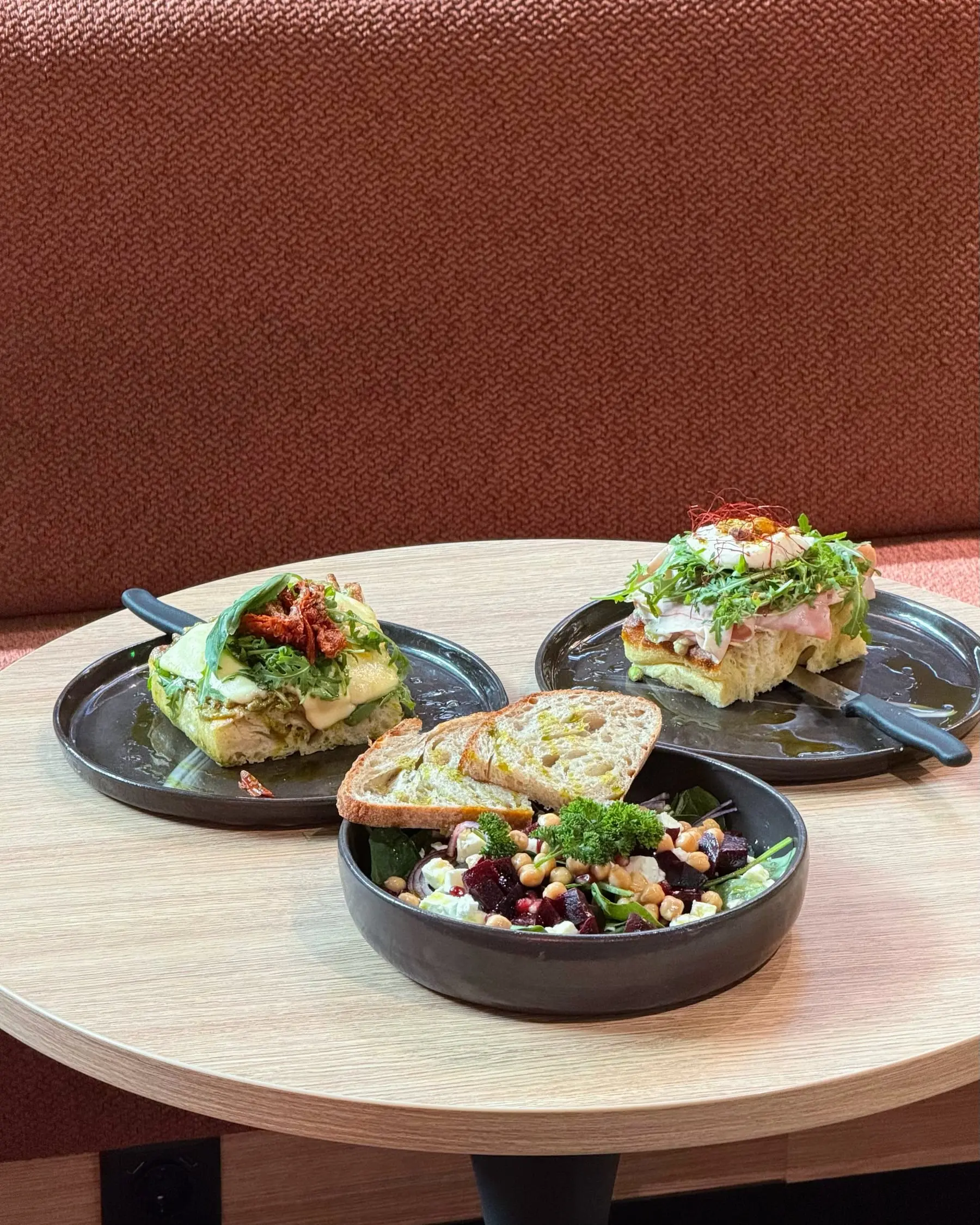 Runder Holztisch mit Bowl, Focaccia und belegtem Brot vor einer terrakottafarbenen Sitzbank