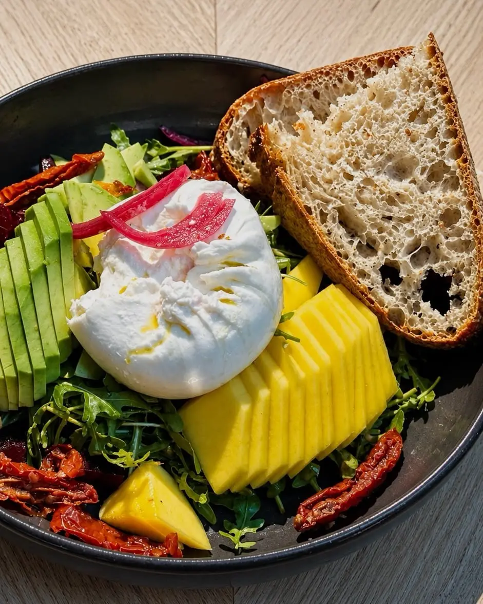 Bowl mit Burrata, Avocado, Mango, getrockneten Tomaten und Sauerteigbrot