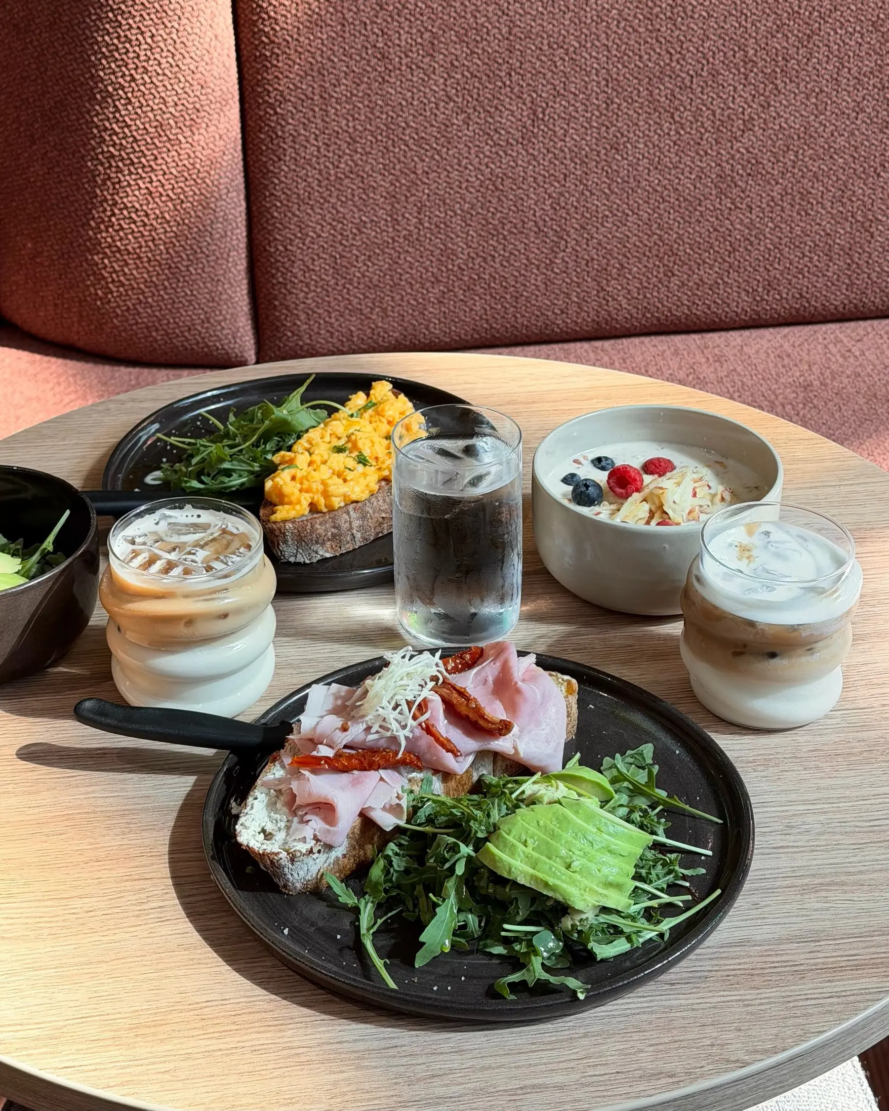 Frühstück mit Schinken, Rührei, Avocado, Joghurt mit Beeren und Iced Latte